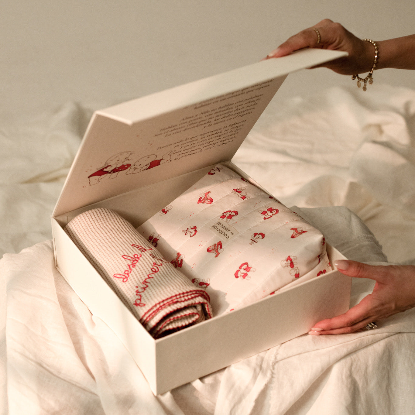 Manos abriendo la caja premium de Alma y Nilo con la cobija y la bolsita visibles dentro