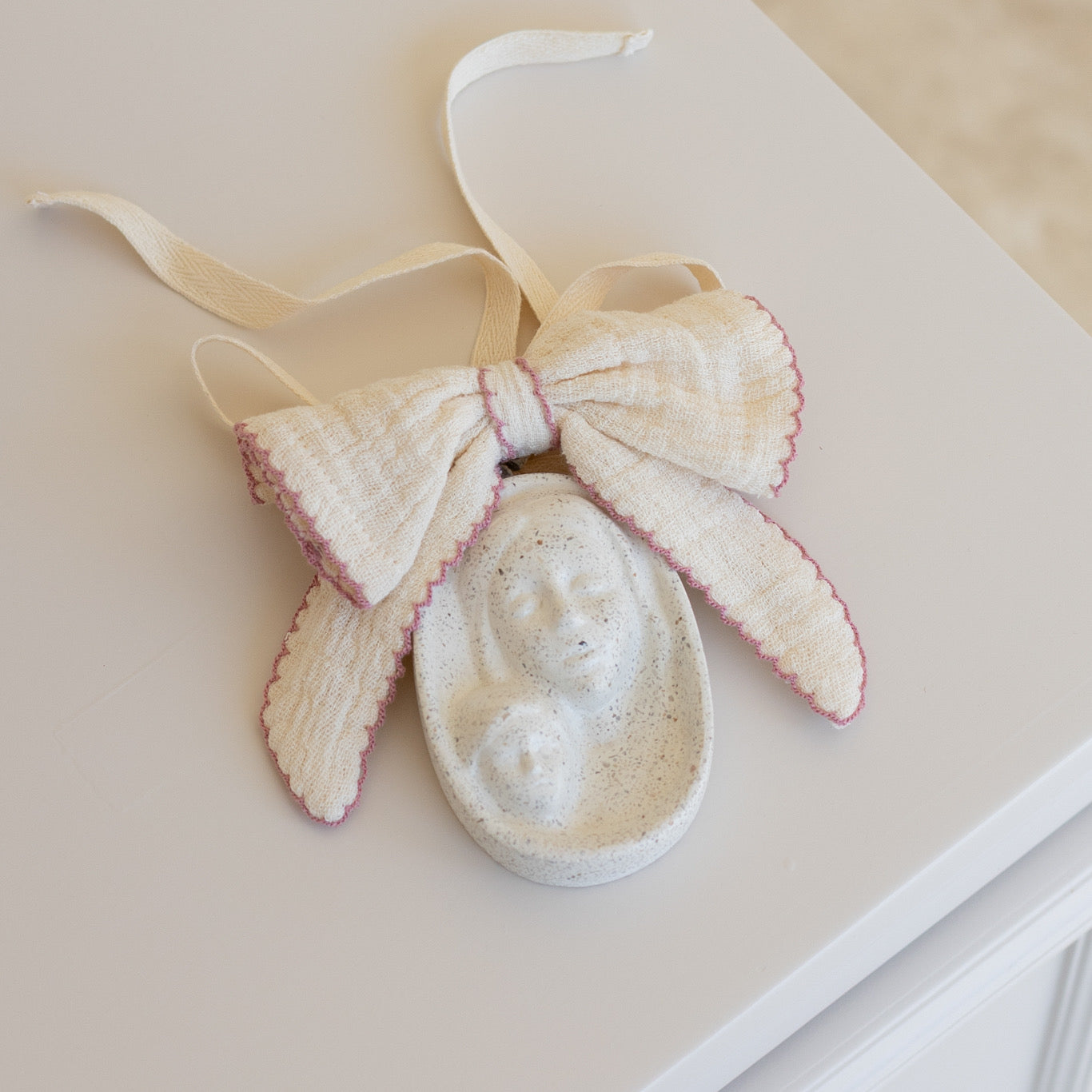 Bendición de cuna personalizada con moño orilla color rosa colocada sobre superficie clara, medalla decorativa para bebé