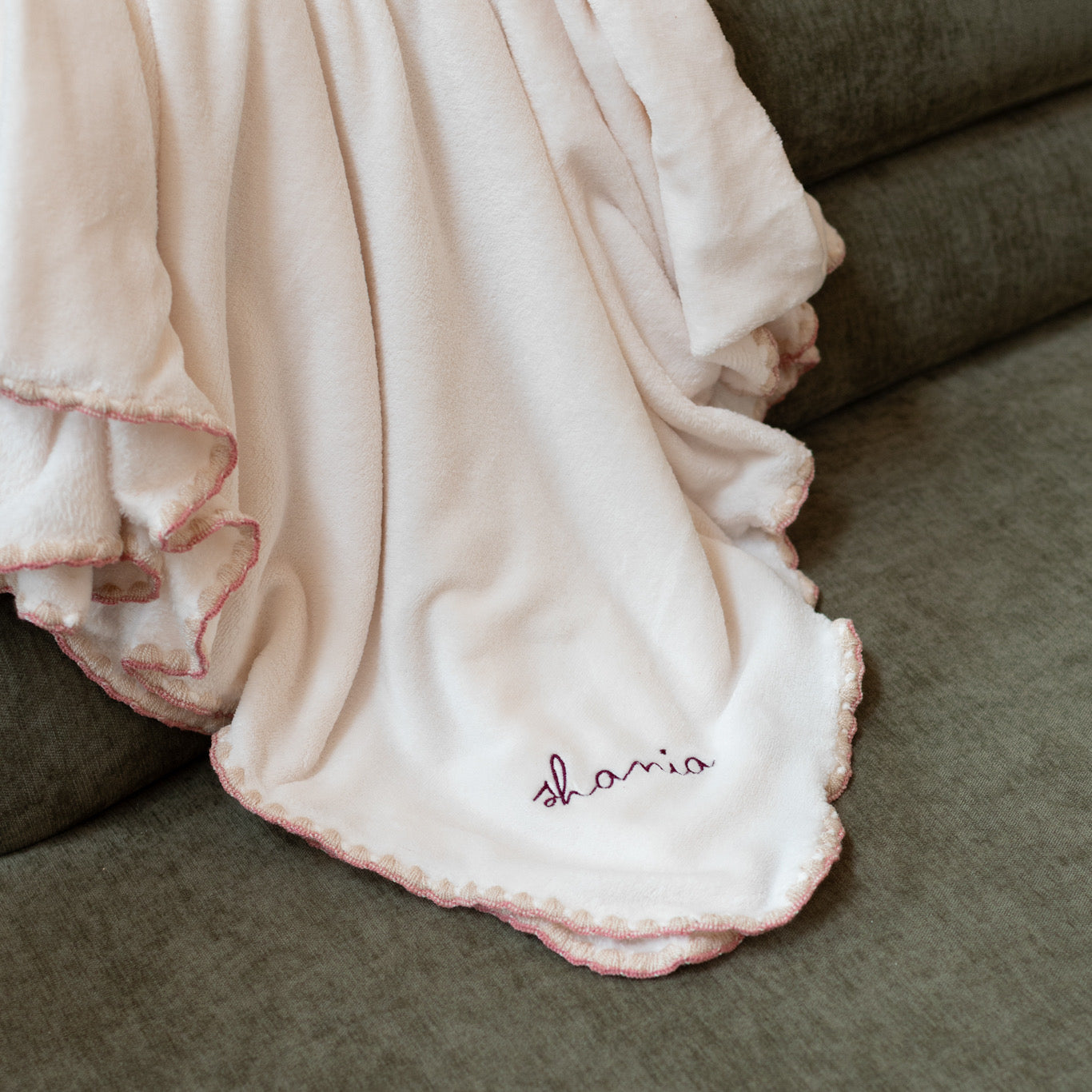 Cobija Caricia polar para bebé personalizada con bordado borgoña y orilla rosa sobre sillón