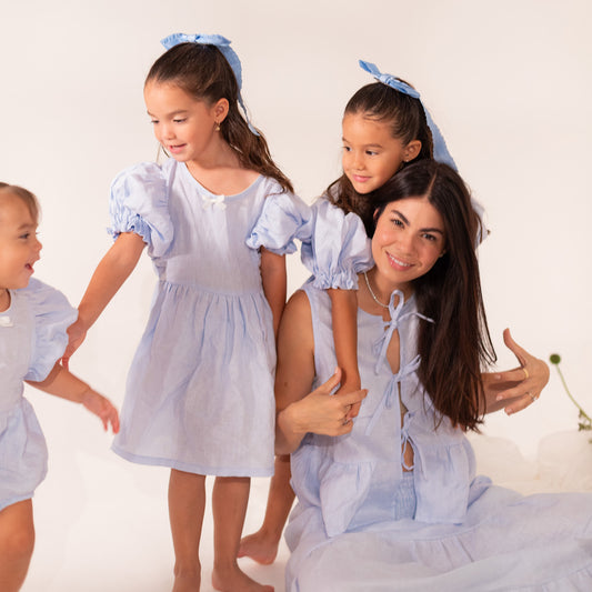 Mamá con top de tres lazos de lino en color azul cielo combinando con sus hijas y bebé en prendas de lino a juego