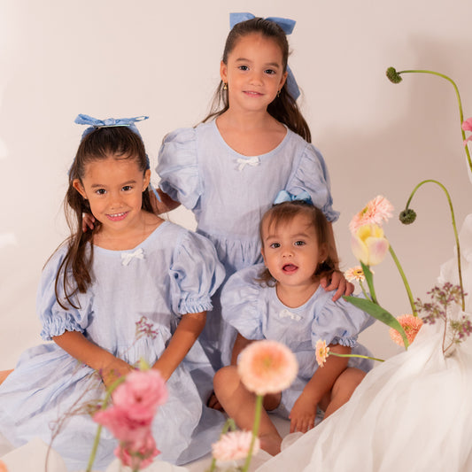 Dos niñas con Vestido Bombón y una bebé con Enterizo Bombón de lino en color azul cielo durante una sesión de fotos